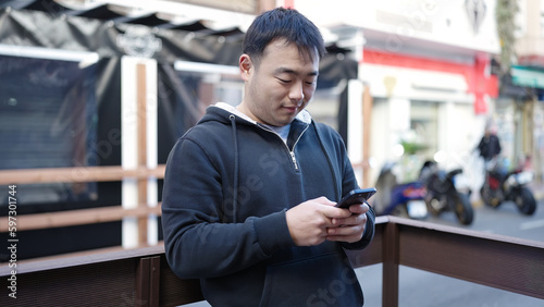 Young chinese man using smartphone with relaxed expression at street