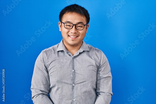 Young chinese man standing over blue background with a happy and cool smile on face. lucky person.