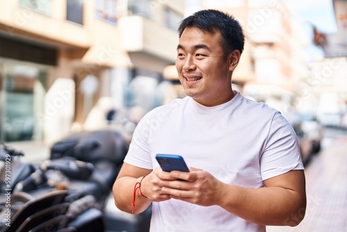 Young chinese man smiling confident using smartphone at street © Krakenimages.com
