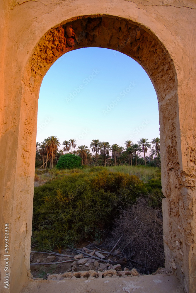 Arab historical building consisting of columns and windows made of clay and rocks, overlooking a nature of palm trees and green trees
