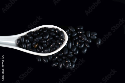 White ceramic spoon full of black beans isolated on black background.