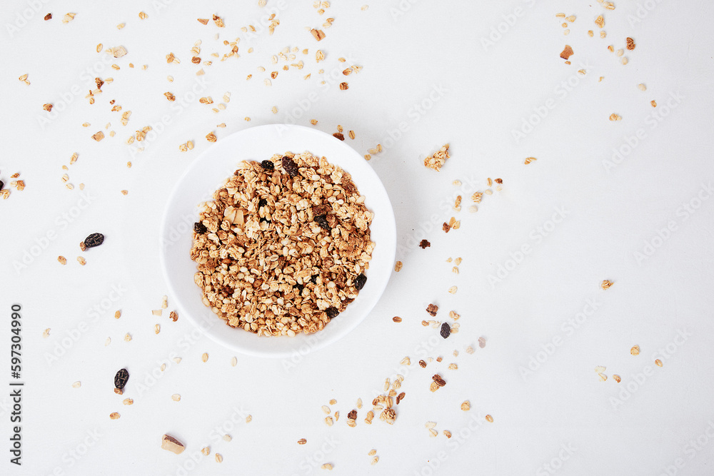 A bowl of granola sits on a white table with scattered granola on it. A bowl of granola sits on a white table with scattered granola on it.
