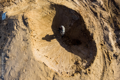 Top view of a man standing in a sandy hole that looks like a lunar crater