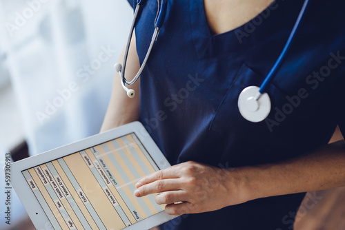 Doctor woman using tablet computer while standing near panorama window in clinic, close up. Physician or surgeon at work. Medicine concept photo