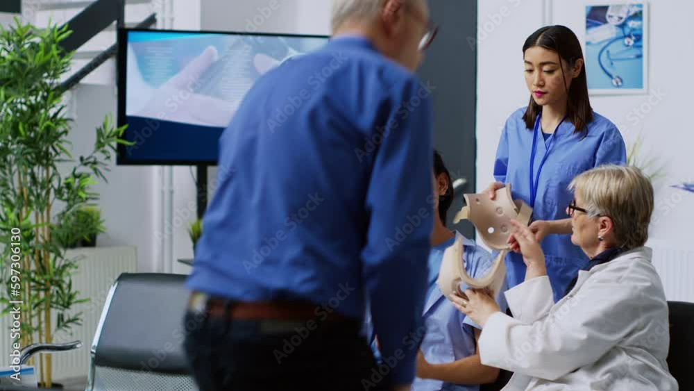 Physician medic helping injured patient to take off cervical collar during checkup visit consultation in hospital waiting room. Asian man having neck injury receiving help from medical staff Physician medic helping injured patient to take off cervical collar during checkup visit consultation in hospital waiting room. Asian man having neck injury receiving help from medical staff