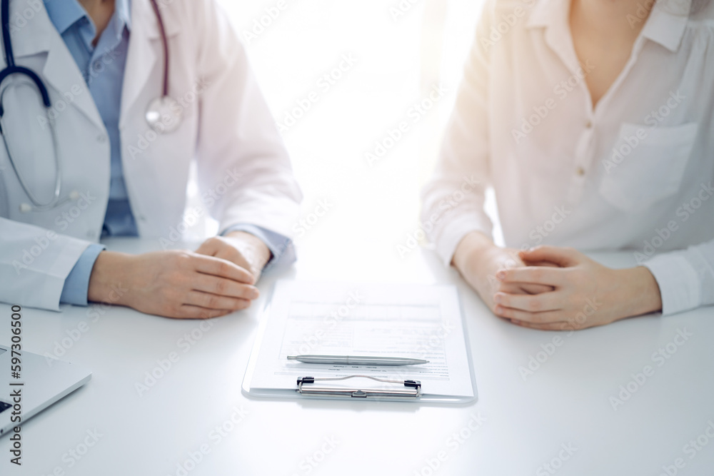 Doctor and patient discussing current health questions while sitting near of each other and using clipboard at the table in clinic, just hands closeup. Medicine concept