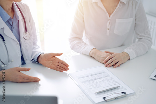 Fototapeta Naklejka Na Ścianę i Meble -  Doctor and patient discussing current health questions while sitting near of each other and using clipboard at the table in clinic, just hands closeup. Medicine concept