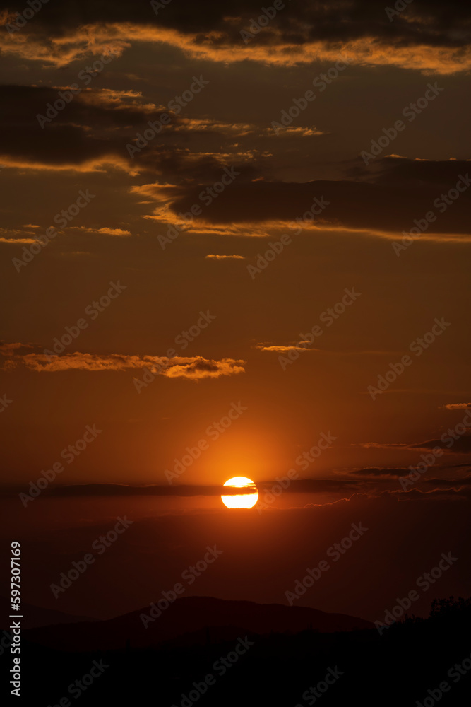 Sunset in the mountain. Panoramic view of unique mountain landscape at sunset with big rocks in the foreground. The sun falls for horizon, a sunset. Shadows are condensed, beautiful clouds.