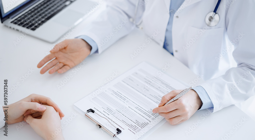Doctor and patient discussing current health questions while sitting opposite of each other and using clipboard at the table in clinic, just hands closeup. Medicine concept Doctor and patient discussing current health questions while sitting opposite of each other and using clipboard at the table in clinic, just hands closeup. Medicine concept