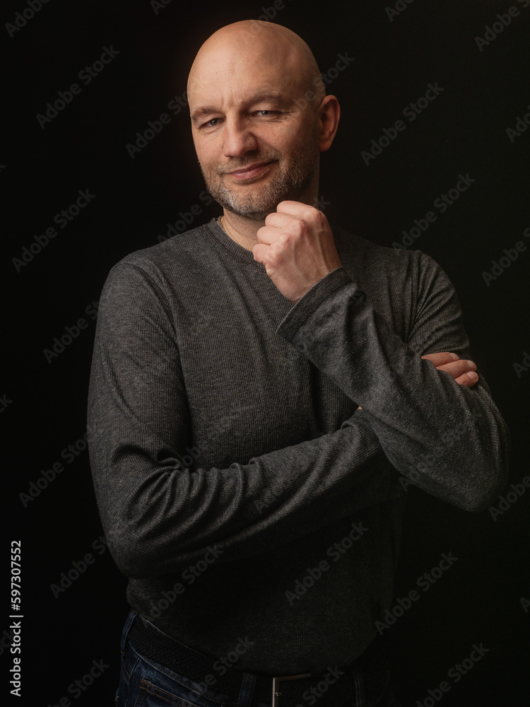 Portrait of a bald man in his 40s in grey shirt, smile on his face, dark background. Slim body type.