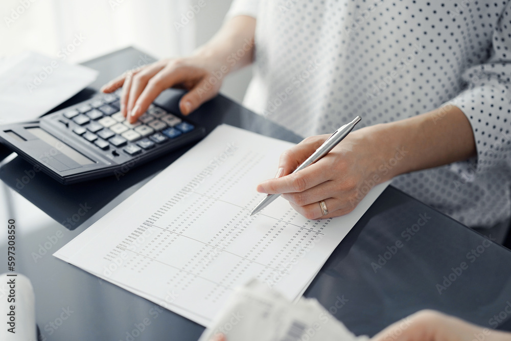 Woman accountant using a calculator and laptop computer while counting taxes for a client. Business audit and finance concepts Woman accountant using a calculator and laptop computer while counting taxes for a client. Business audit and finance concepts
