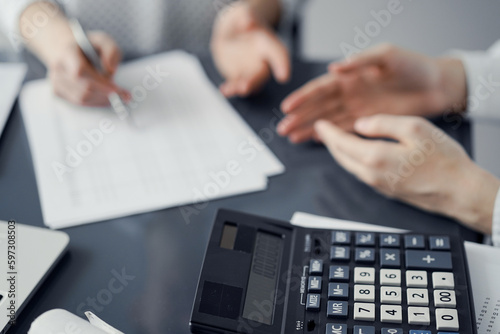 Woman accountant using a pen and laptop computer while counting and discussing taxes with a client  focus on the calculator. Business audit and finance concepts