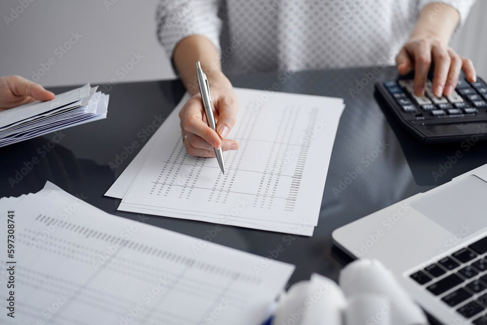 Woman accountant using a calculator and laptop computer while counting taxes for a client. Business audit and finance concepts Woman accountant using a calculator and laptop computer while counting taxes for a client. Business audit and finance concepts