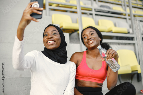 Two black women sitting on a stairs on a stadium after doing workout and make a selfie