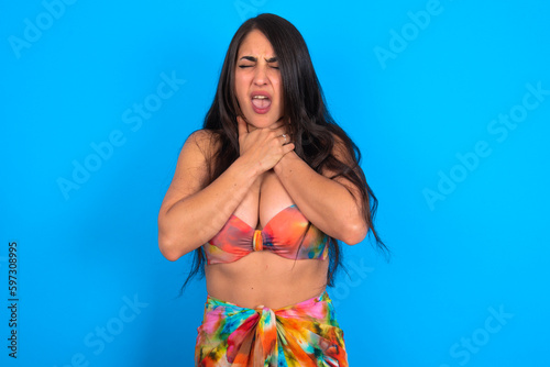 beautiful brunette woman wearing swimwear over blue background shouting suffocate because painful strangle. Health problem. Asphyxiate and suicide concept.