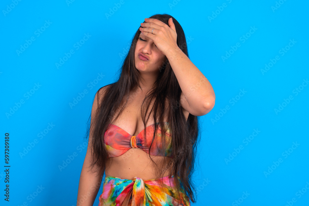 A very upset and lonely beautiful brunette woman wearing swimwear over blue background crying,