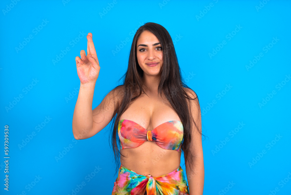 beautiful brunette woman wearing swimwear over blue background pointing up with fingers number ten in Chinese sign language Shi