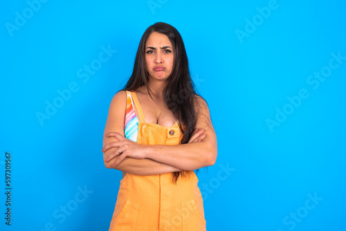 Obraz na plátně Gloomy dissatisfied brunette woman wearing orange overalls over blue studio back