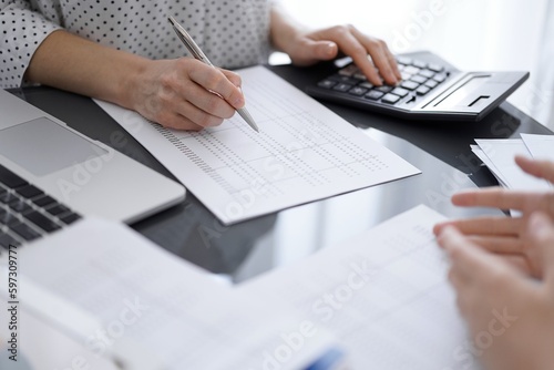 Woman accountant counting and discussing taxes with a client or a colleague while using a calculator and laptop computer. Business audit team