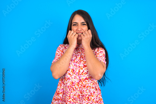 Terrified beautiful brunette woman wearing floral dress over blue background looks empty space home alone moonless night