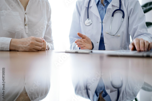 Doctor and patient discussing something while using laptop computer and sitting near each other at the wooden desk in clinic. Medicine concept