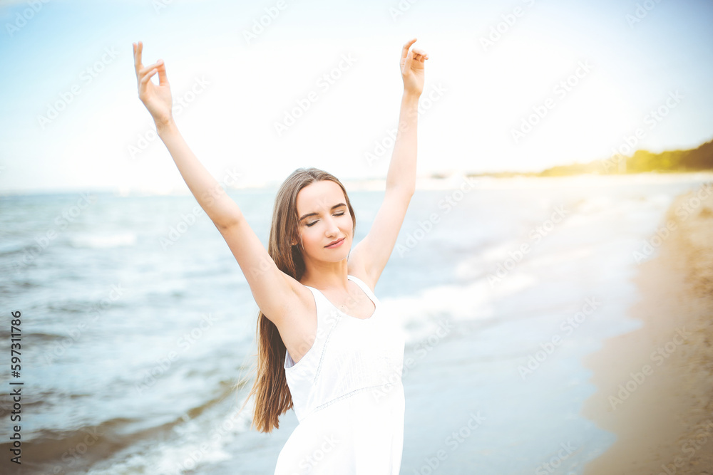 Happy smiling woman in free happiness bliss on ocean beach standing with raising hands. Portrait of a multicultural female model in white summer dress enjoying nature Happy smiling woman in free happiness bliss on ocean beach standing with raising hands. Portrait of a multicultural female model in white summer dress enjoying nature