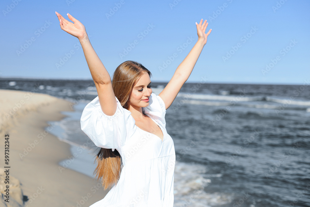 Happy, beautiful woman on the ocean beach standing in a white summer dress, raising hands Happy, beautiful woman on the ocean beach standing in a white summer dress, raising hands