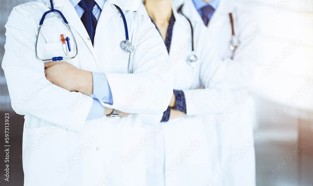 Group of modern doctors standing as a team with crossed arms and stethoscopes in a sunny hospital office. Physicians ready to examine and help patients.