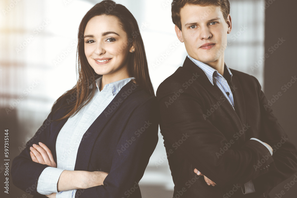 Friendly young colleagues are standing as a team with crossed arms in sunny office. Successful business people at work Friendly young colleagues are standing as a team with crossed arms in sunny office. Successful business people at work