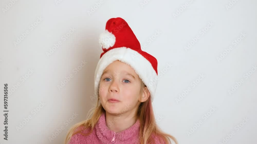 A little blond girl in red Santa Claus hat is actively telling something and looking at the camera. The girl sings or recites a poem. Video portrait. 4k resolution video. A little blond girl in red Santa Claus hat is actively telling something and looking at the camera. The girl sings or recites a poem. Video portrait. 4k resolution video.