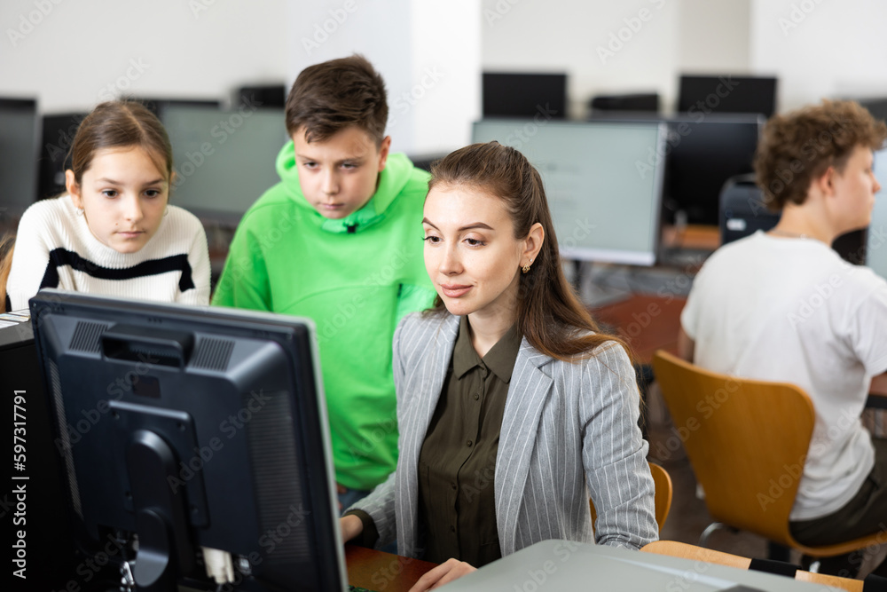 Fototapeta premium Interested teenagers studying with young female teacher in information technology class at college, sitting around one computer