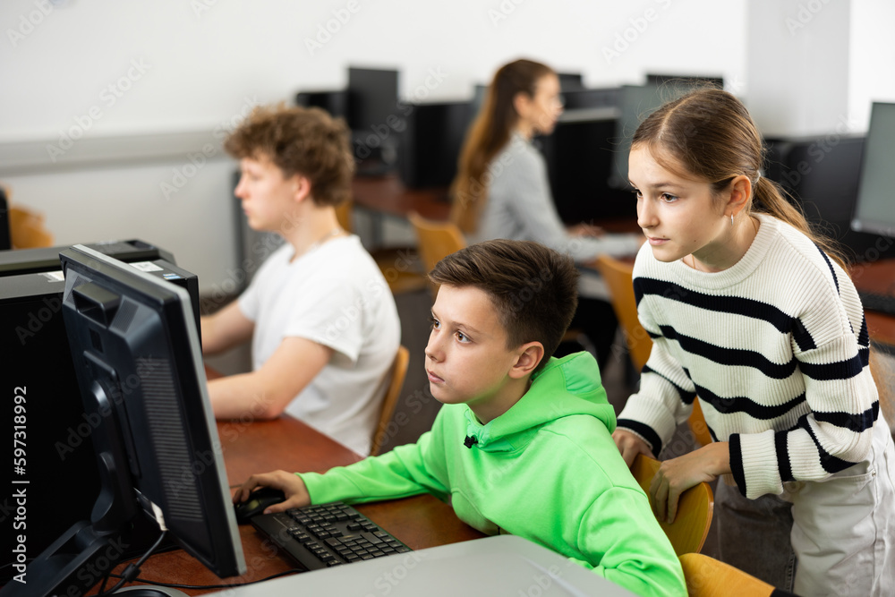 Fototapeta premium Positive female teacher helping focused preteen schoolboy studying in college library computer lab..