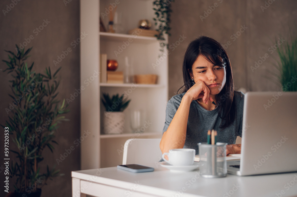Tired young woman staring at the laptop screen while working in her home office.