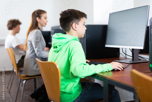 Young boy sitting at table and using computer during lesson.