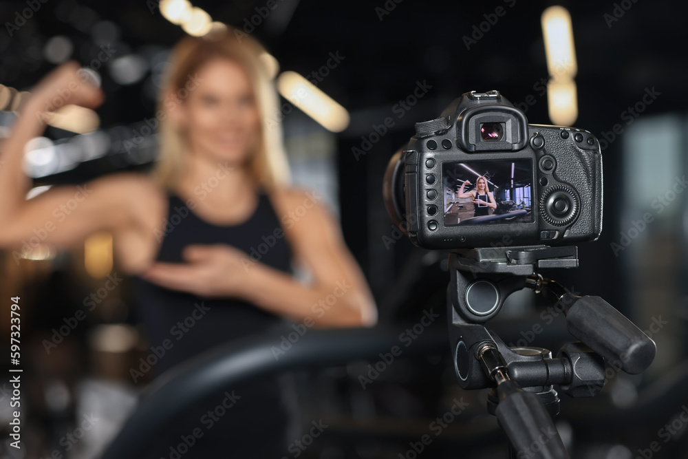 Fitness trainer recording online classes in gym, focus on camera. Space for text