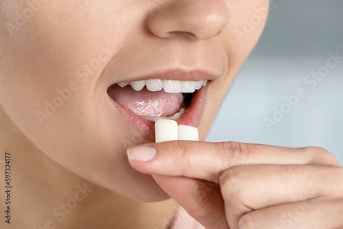 Woman putting chewing gums into mouth on blurred background, closeup