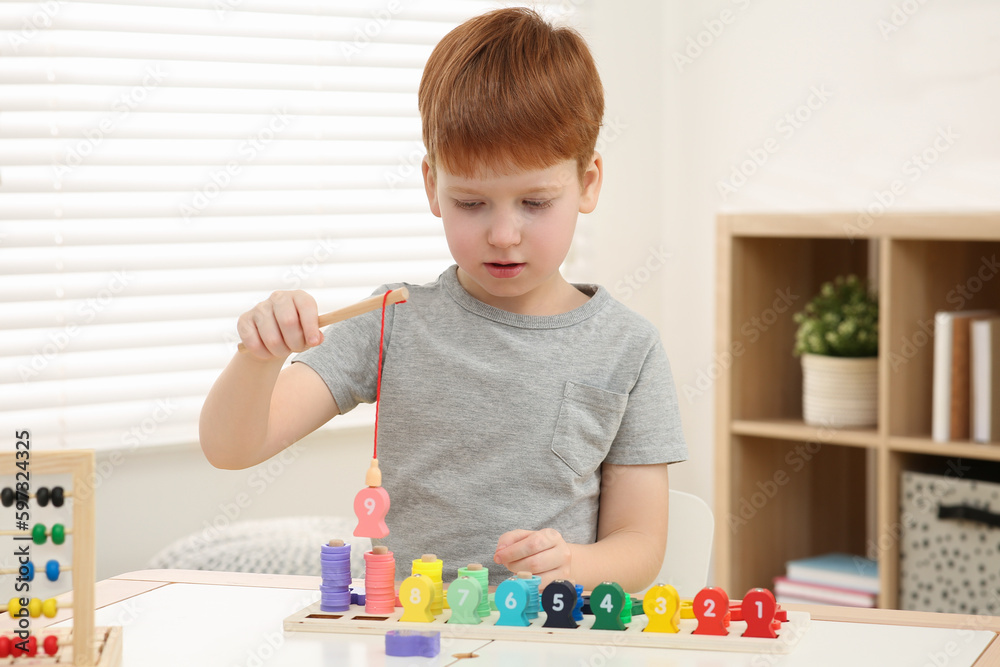Fototapeta premium Little boy playing with Educational game Fishing for Numbers at desk in room. Learning mathematics with fun