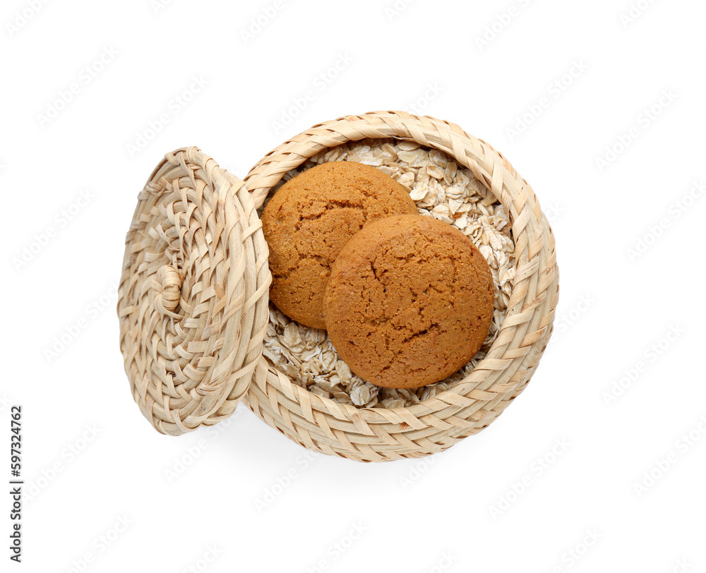 Wicker basket with delicious oatmeal cookies and flakes on white background, top view