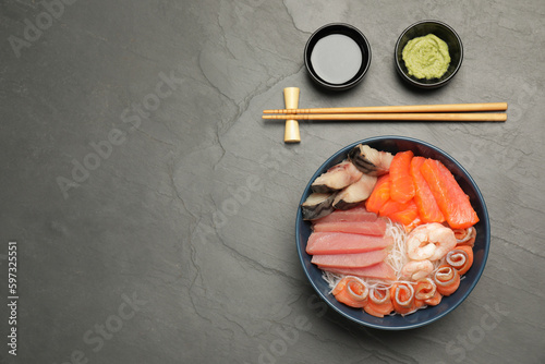 Delicious mackerel, salmon, shrimps and tuna served with funchosa, wasabi and soy sauce on grey table, flat lay with space for text. Tasty sashimi dish