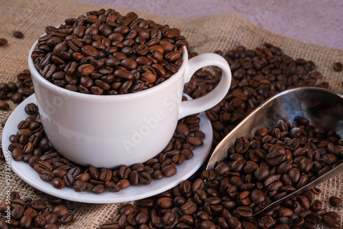 Close-up of white cup with coffee beans and metal shovel