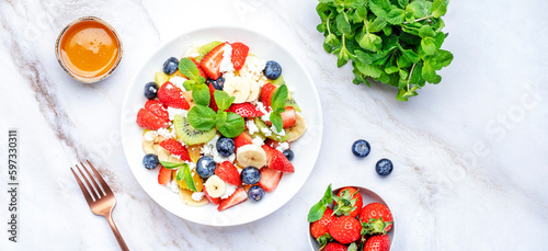 Summer fruit and berry salad with cottage cheese and mint leaves with honey dressing, marble table background, top view