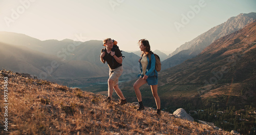 Caucasian couple hiking together with backpacks, helping each other on their way up the mountains - freedom, active lifestyle concept 