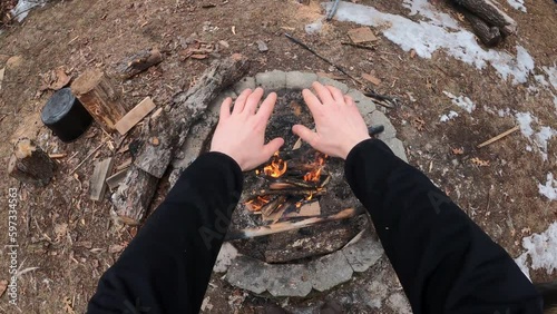 Pullin hand over fire pit getting warm while burning wood in back yard. First person view. photo