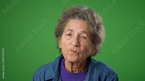 Fotografia Closeup portrait of thinking thoughtful toothless elderly old toothless woman with tongue out on green screen background