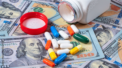 Pills and tablets spilling out of a white plastic bottle on US dollar banknote. Pharmacy concept.