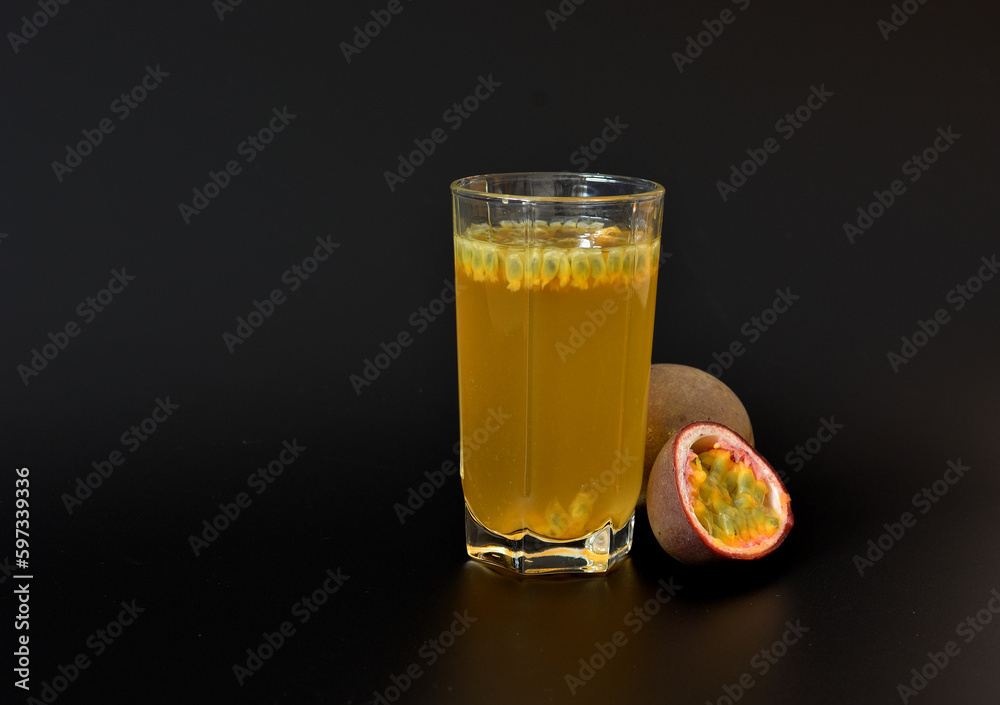 A glass of freshly squeezed fruit juice with seeds and slices of ripe passion fruit on a black background.