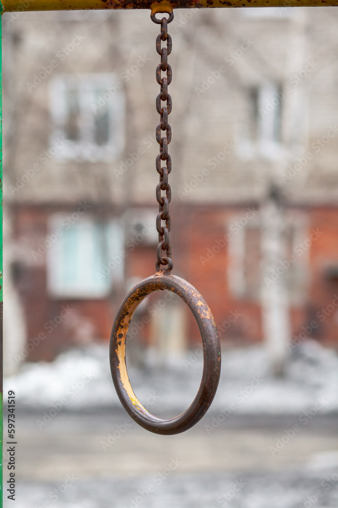 An iron chain with gray and translucent oval rings on a gray background in the courtyard of a multi-storey building. A place of rest and activities for children
