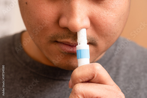 A man using a menthol inhaler to treat a stuffy nose. Sniffing an inhaler and sticking it up his nose.  photo