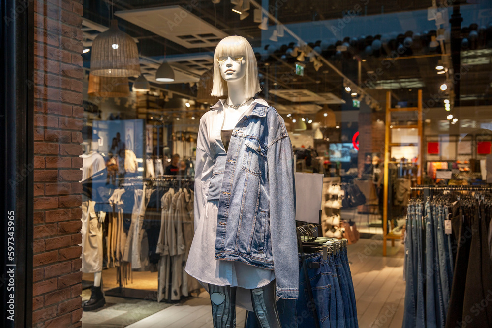 A female mannequin in a denim jacket in a glass showcase of a fashionable youth clothing store. Style and beauty. Close-up. A female mannequin in a denim jacket in a glass showcase of a fashionable youth clothing store. Style and beauty. Close-up.
