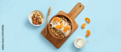 Tasty granola with yogurt and tangerines in bowl on light blue background